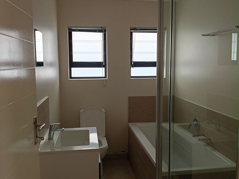 A clean, modern bathroom featuring a vanity basin, bathtub, and separate glass shower enclosure with neutral tiling throughout.