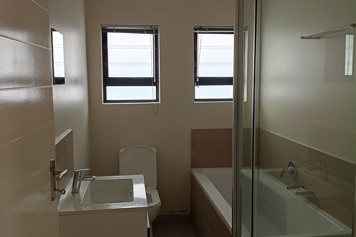 A clean, modern bathroom featuring a vanity basin, bathtub, and separate glass shower enclosure with neutral tiling throughout.