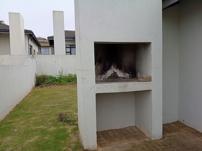 Rear garden area featuring a built-in masonry braai, paved patio section, and perimeter boundary walls.