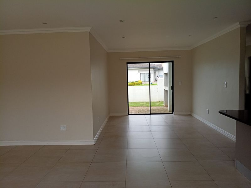 Spacious open-plan living area featuring neutral tiled flooring, recessed lighting, and a sliding glass door providing direct access to the rear garden.