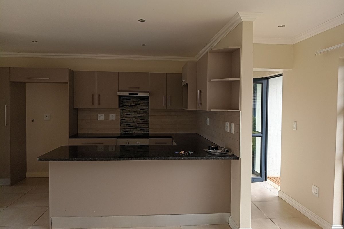 A clean, modern kitchen featuring granite countertops, built-in cabinetry, a hob with extractor fan, and neutral tiled flooring in an open-plan layout.