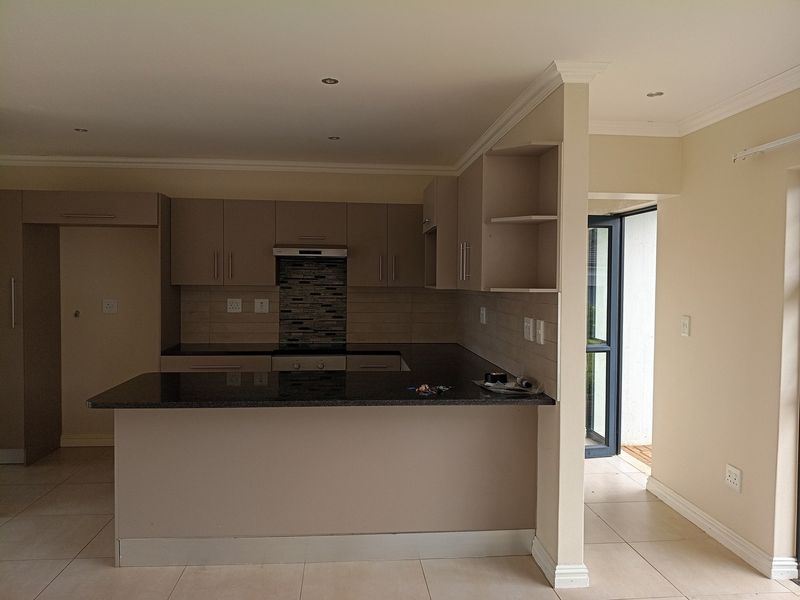 A clean, modern kitchen featuring granite countertops, built-in cabinetry, a hob with extractor fan, and neutral tiled flooring in an open-plan layout.