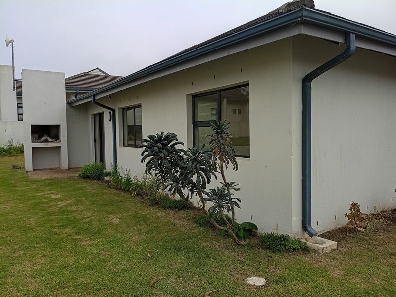 Rear exterior view of the property featuring a built-in braai, lawn area, and modern aluminium window frames with standard guttering system.