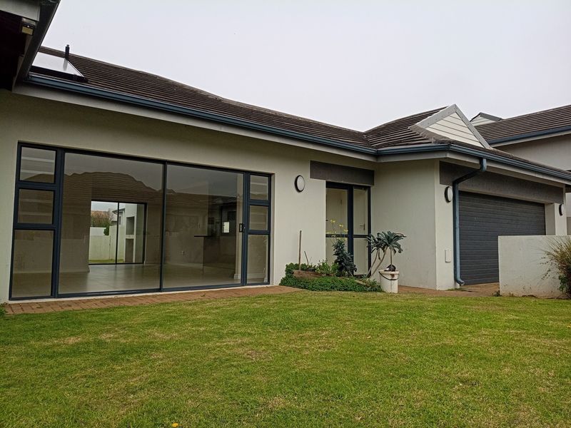 Rear view of the property featuring a paved patio area, large sliding glass doors, and an attached double garage with a well-maintained lawn.