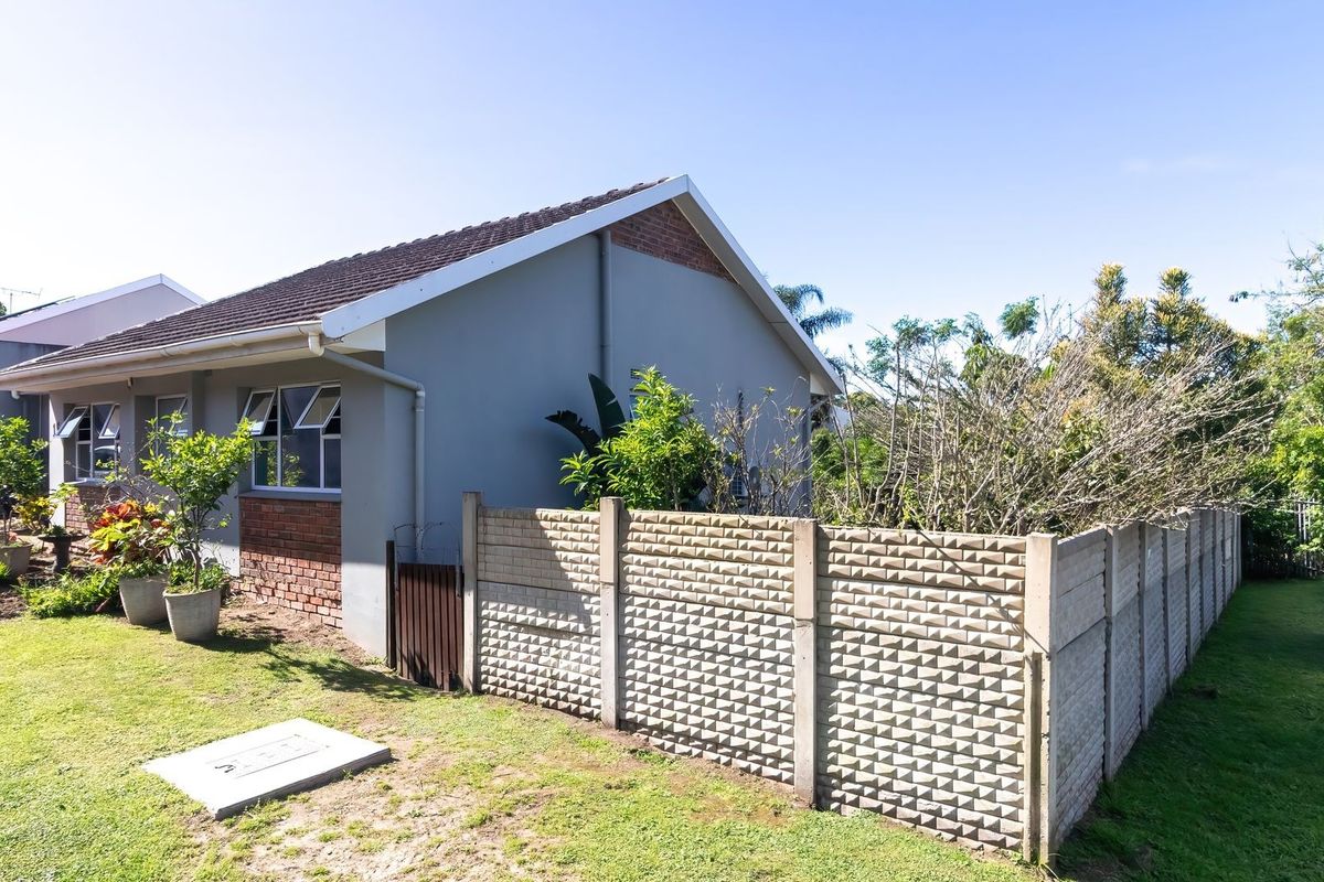 Rear view of the townhouse featuring a tiled roof, brick and plaster exterior, and a precast concrete boundary wall with surrounding garden space.