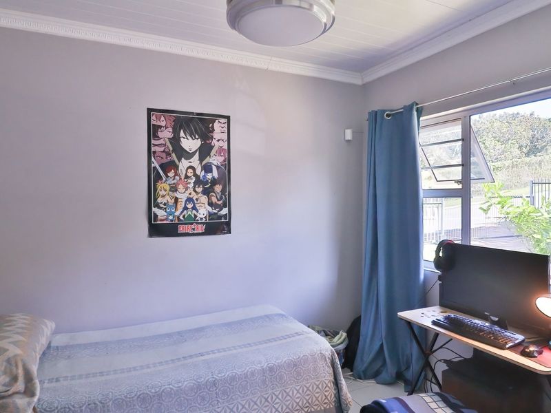 A functional bedroom featuring tiled flooring, a tongue and groove ceiling with decorative cornice, and large aluminium-framed windows allowing natural light.