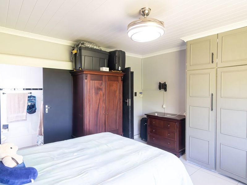 A bedroom featuring built-in cupboards, tiled flooring, a ceiling fan, and direct access to an en-suite bathroom.