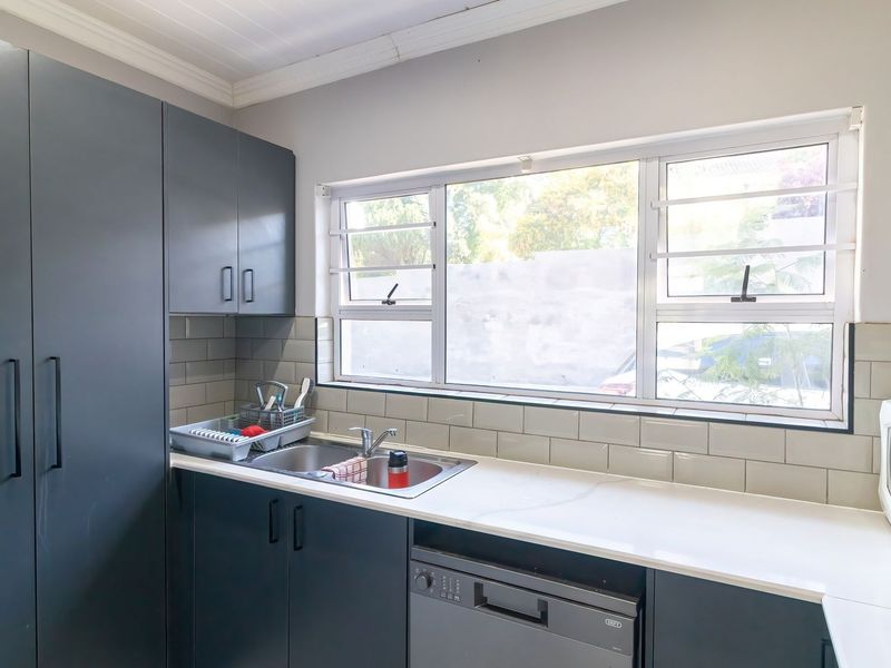 Modern kitchen featuring dark cabinetry, stone countertops, a stainless steel double sink, and a subway tile backsplash with ample natural light.
