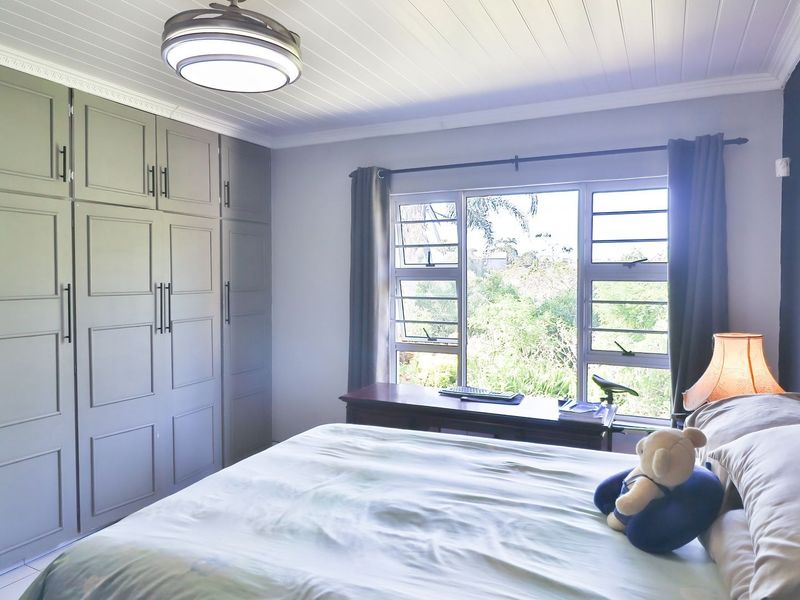 A well-maintained bedroom featuring built-in cupboards, a tongue and groove ceiling, air conditioning, and louvered windows overlooking a garden.
