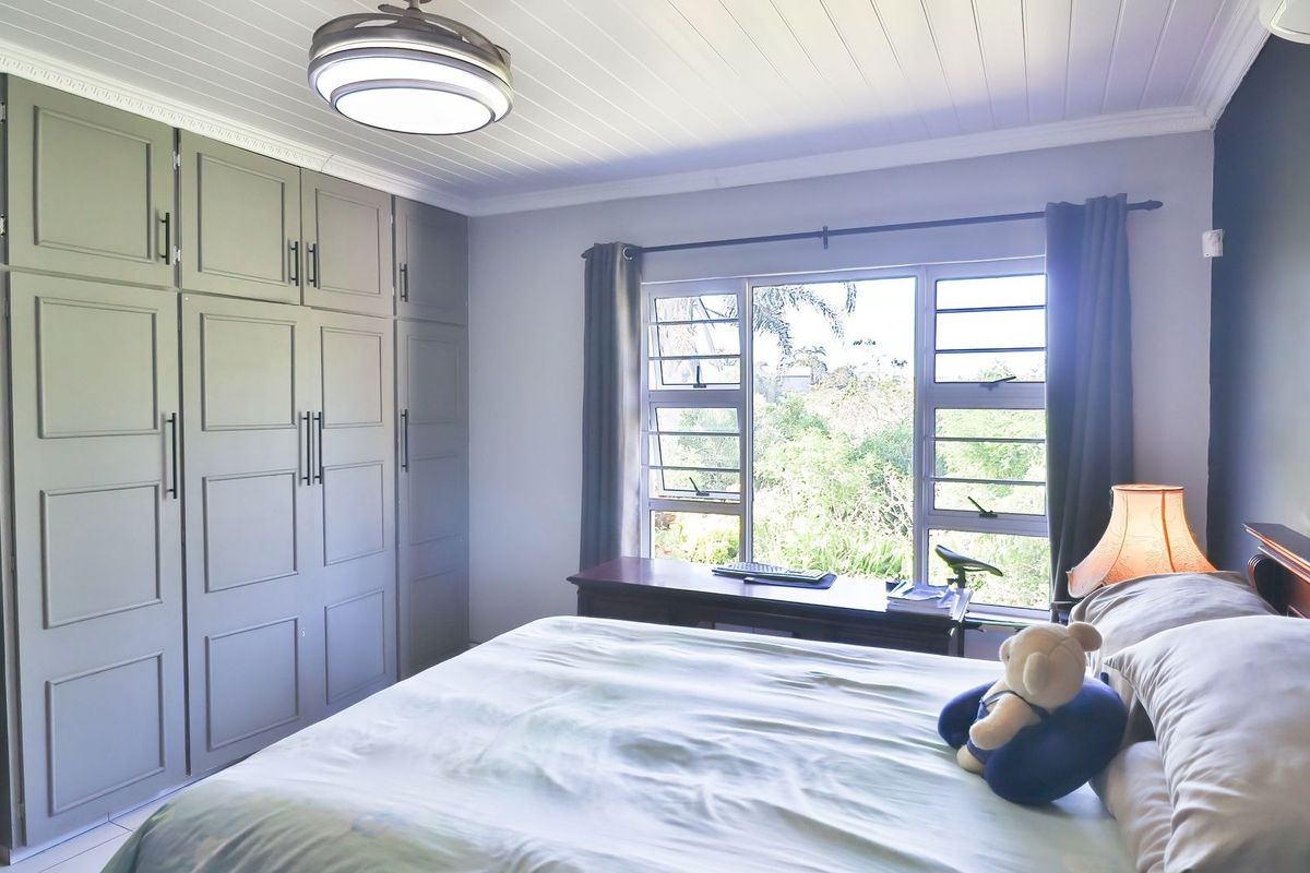 A well-maintained bedroom featuring built-in cupboards, a tongue and groove ceiling, air conditioning, and louvered windows overlooking a garden.