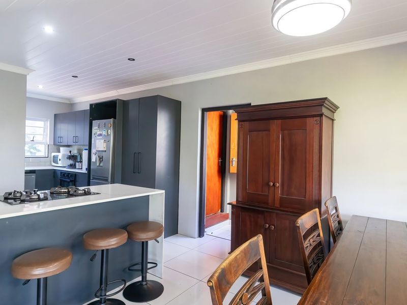 Modern open-plan kitchen and dining area featuring dark cabinetry, stone countertops, a gas hob, and tiled flooring with clean, contemporary finishes.
