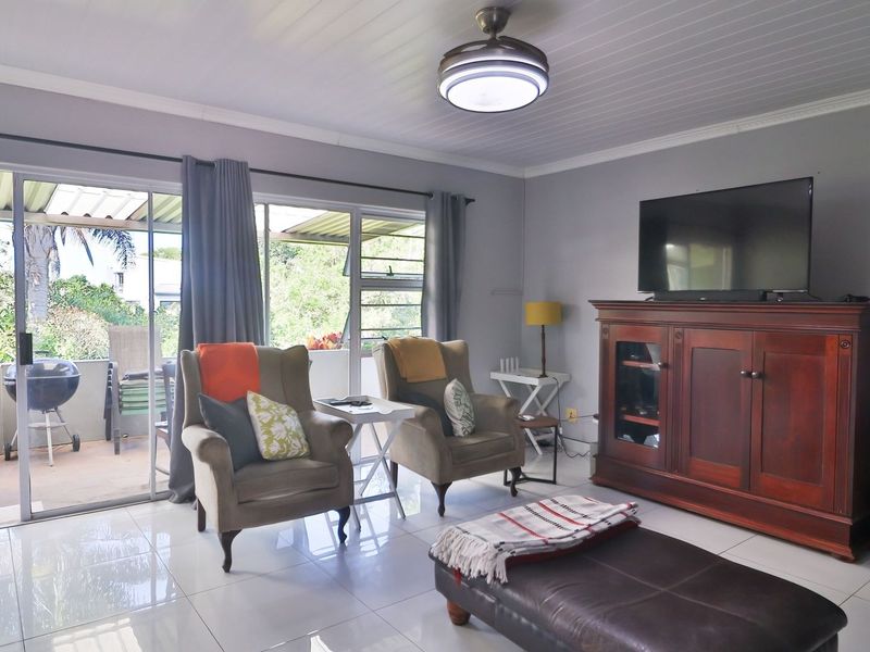 A bright living room featuring large sliding glass doors that open onto a covered patio, complemented by tiled flooring and a ceiling fan.