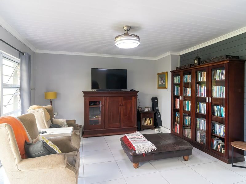 A well-maintained living room featuring tiled flooring, a tongue and groove ceiling, and a decorative accent wall with louver windows.