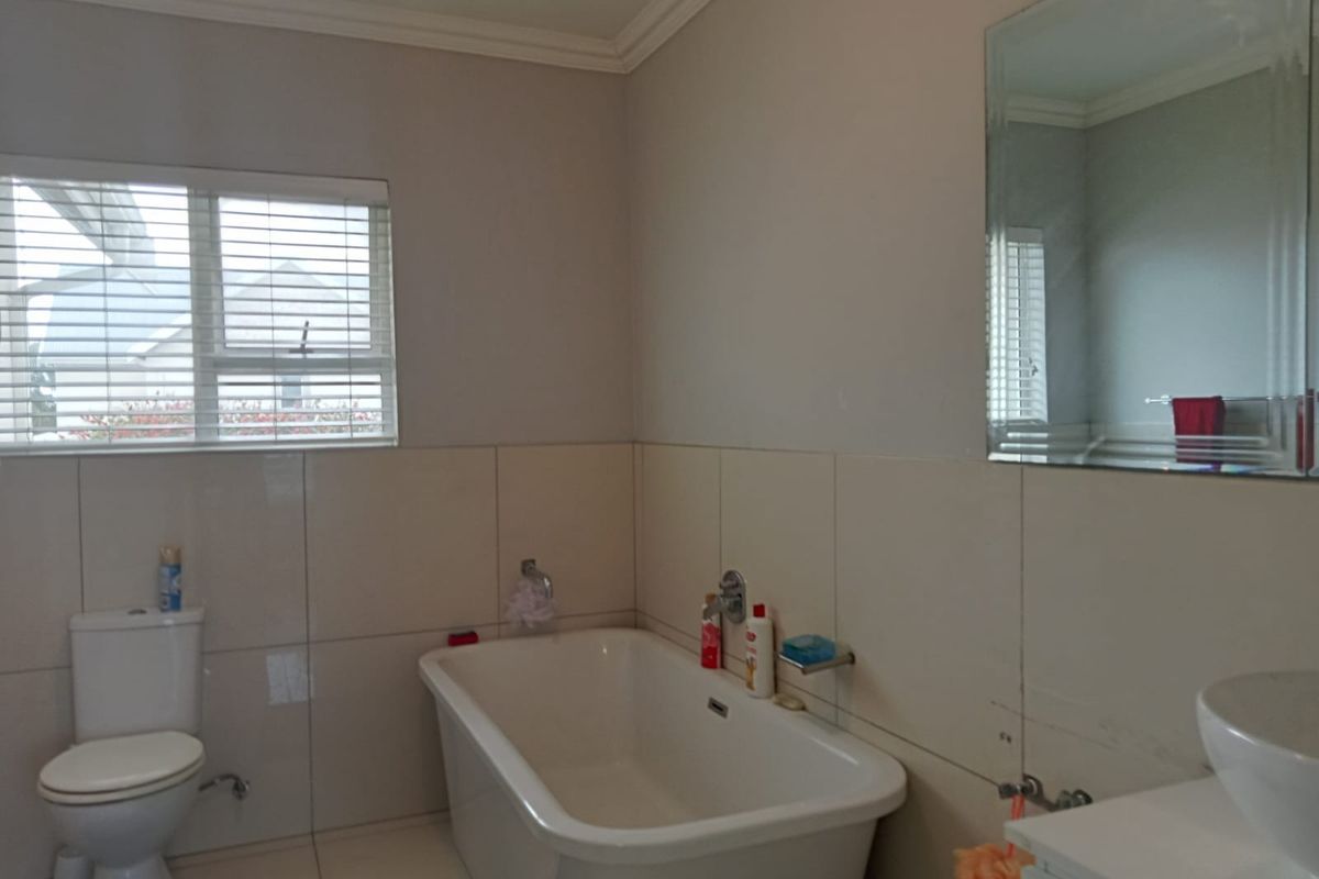 A functional bathroom featuring a freestanding bathtub, wall-mounted toilet, vanity basin, and neutral wall tiling with natural light from the window.