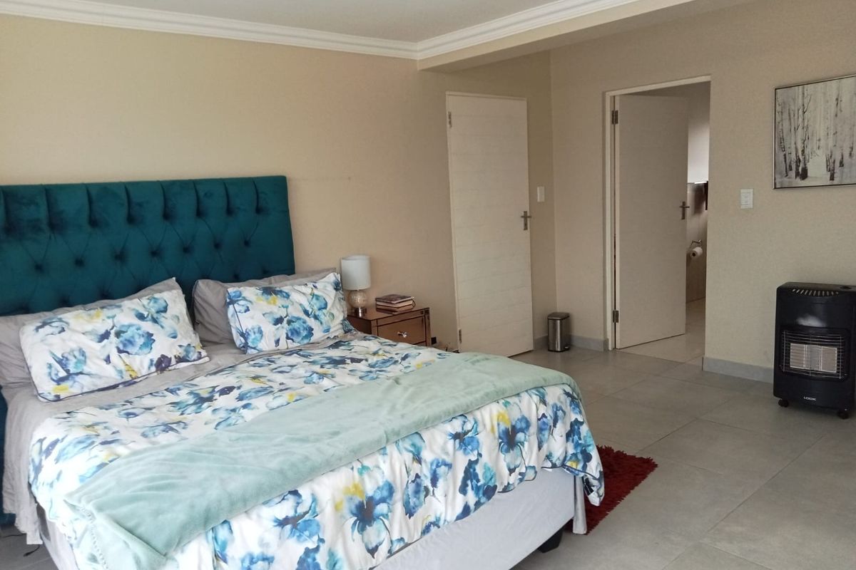 A spacious bedroom featuring neutral wall tones, tiled flooring, and decorative ceiling cornicing, with direct access to an adjoining bathroom.