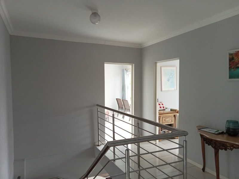 A bright upstairs landing area featuring a modern stainless steel balustrade, tiled flooring, and access to adjacent rooms.