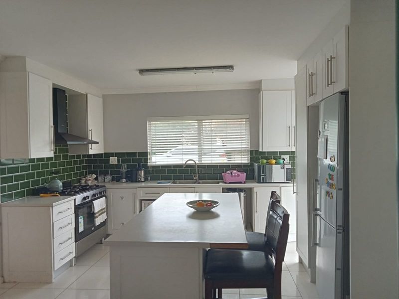 A functional kitchen featuring white cabinetry, a central island, green subway tile backsplash, and a gas stove with an extractor fan.
