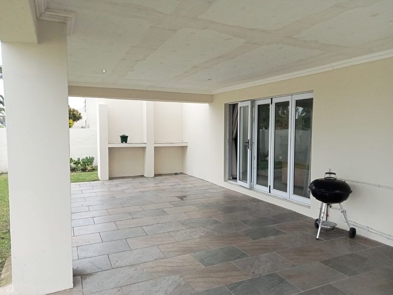 A spacious covered patio featuring tiled flooring, recessed lighting, and built-in masonry shelving, providing direct access to the interior through sliding glass doors.