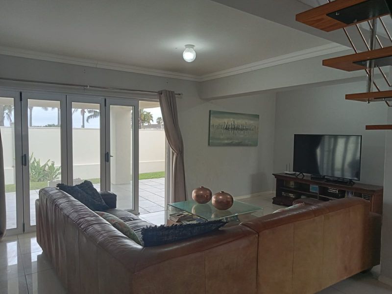 Spacious living room featuring tiled floors, a modern floating staircase, and large sliding glass doors that open onto a patio area.