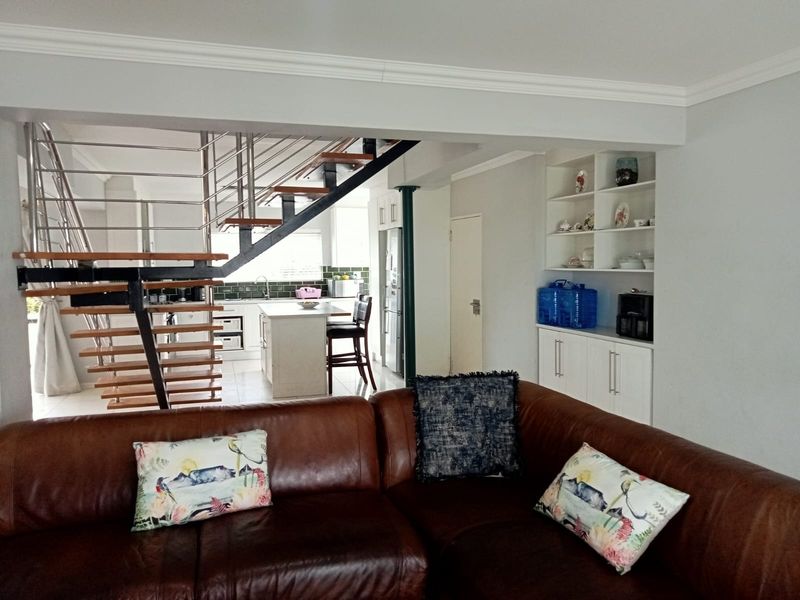 Open-plan living area featuring a modern open-tread staircase with stainless steel balustrades, built-in cabinetry, and a functional kitchen island.