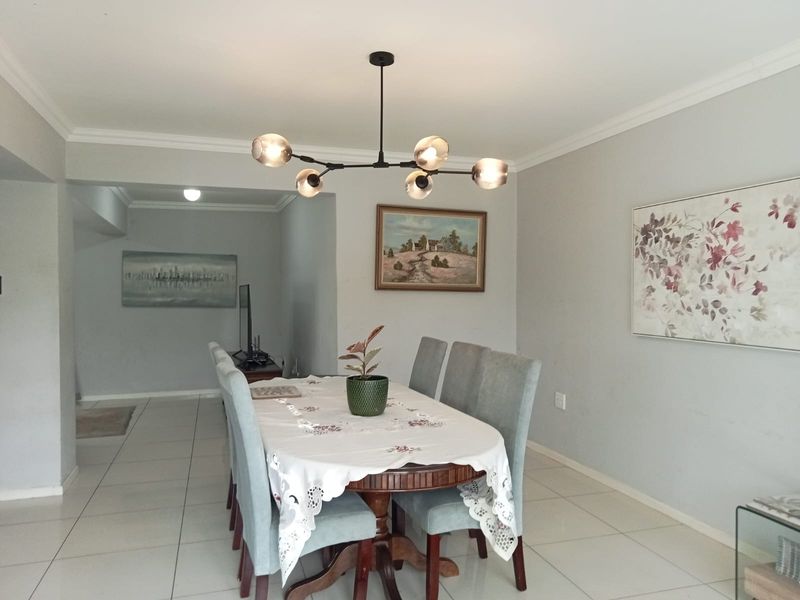 A well-lit dining room featuring neutral tiled flooring, coved ceilings, and a contemporary multi-arm chandelier, creating a bright and inviting space.