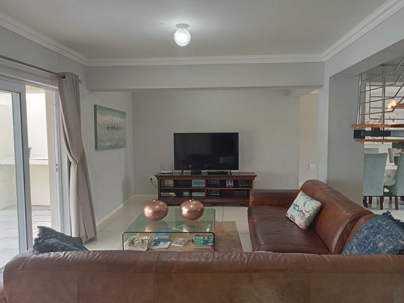 A comfortable living room featuring crown molding, tiled flooring, and a sliding glass door leading to an outdoor area, with an adjacent staircase.