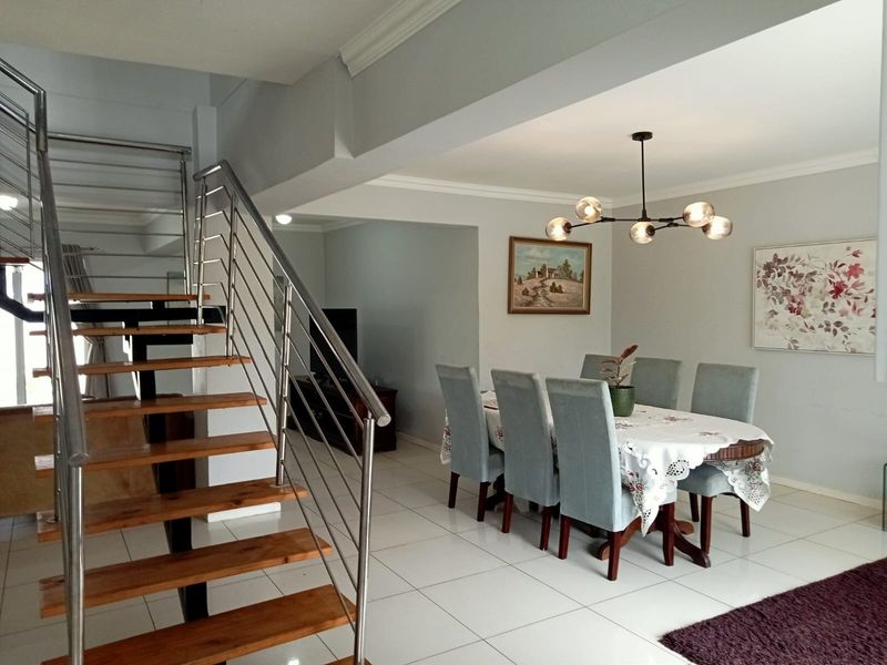 Open plan dining area featuring tiled flooring, modern lighting, and a contemporary staircase with wooden treads and stainless steel balustrades.