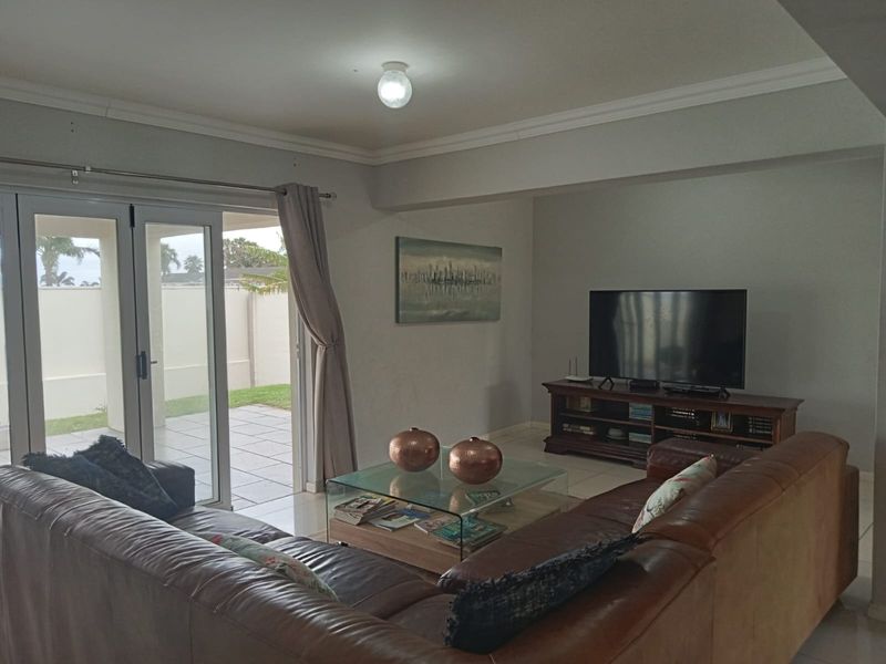Spacious living room featuring tiled flooring, crown molding, and double glass doors providing direct access to the outdoor patio area.