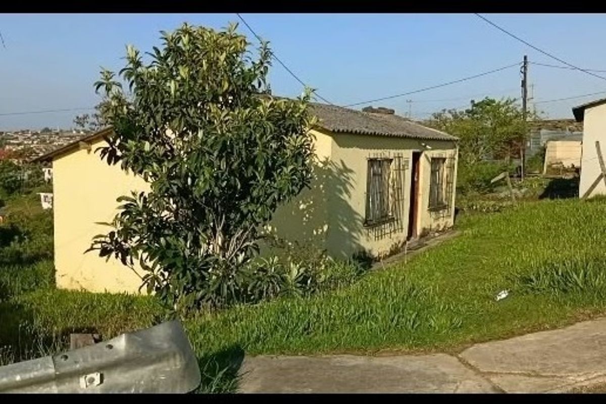 A modest single-story residential house featuring a pitched roof and security bars on windows, situated on a grassed lot.