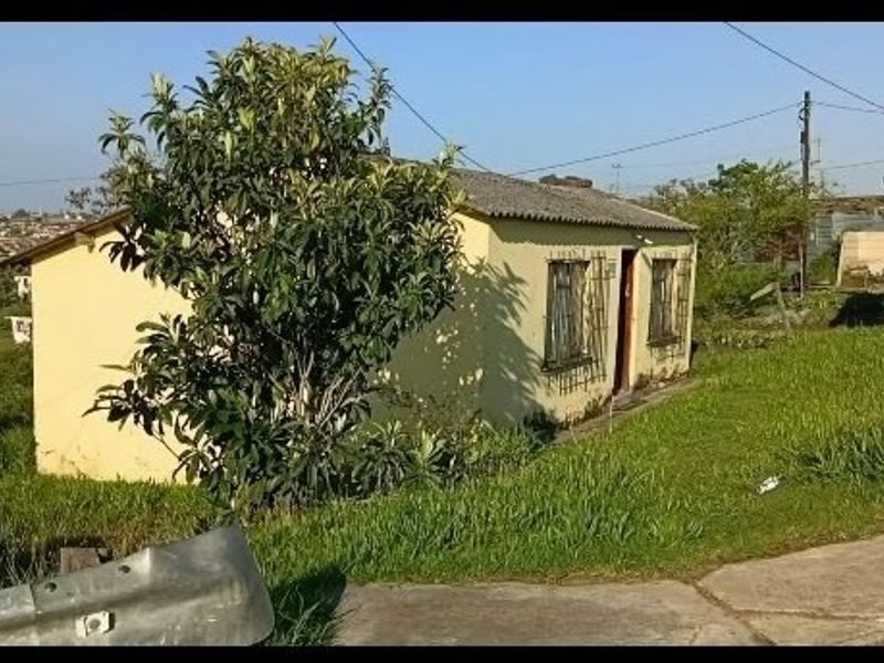 A modest single-story residential house featuring a pitched roof and security bars on windows, situated on a grassed lot.