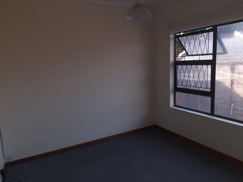 An empty bedroom featuring carpeted flooring, neutral walls, and a window fitted with security bars.