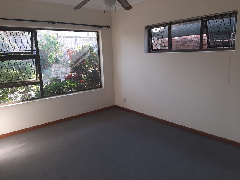 An empty bedroom featuring carpeted flooring, a ceiling fan, and large windows with security burglar bars, offering a blank canvas for potential updates.