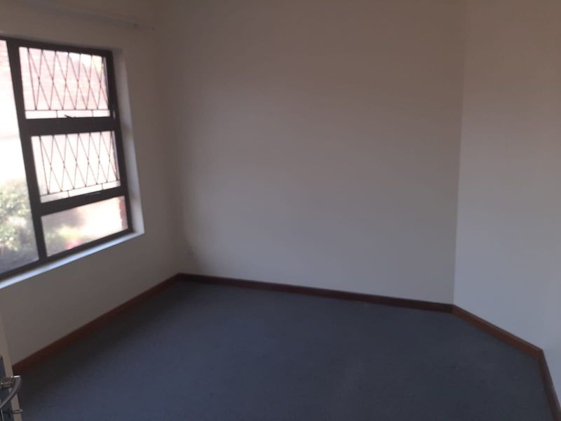 An empty bedroom featuring carpeted flooring and a window fitted with security bars.