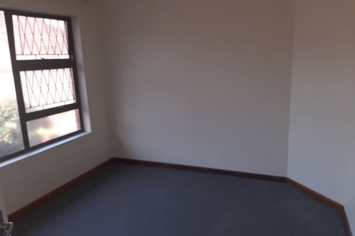 An empty bedroom featuring carpeted flooring and a window fitted with security bars.