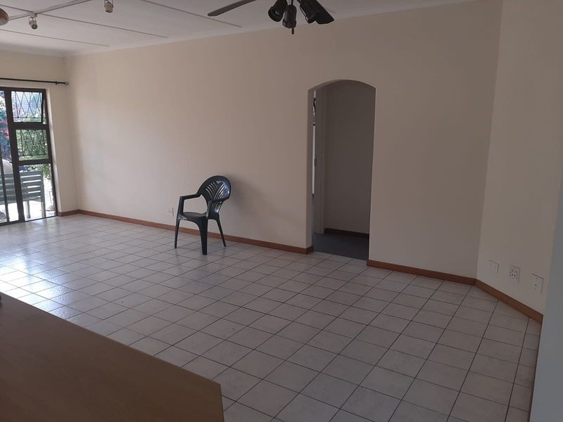 Spacious living area featuring tiled flooring, a ceiling fan, and an arched doorway leading to adjacent rooms, offering a blank canvas for interior design.