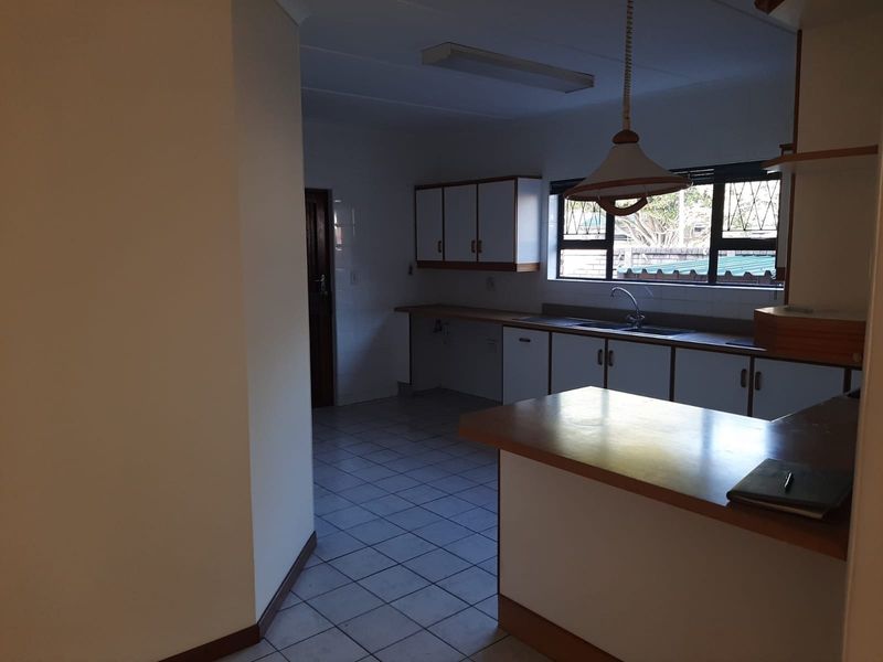 A functional kitchen featuring built-in cabinetry, laminate countertops, a double basin sink, and tiled flooring with a breakfast bar area.