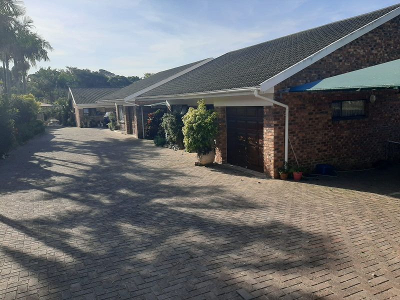 Front exterior view of a townhouse complex featuring a brick facade, tiled roof, and a spacious paved driveway leading to garage entrances.