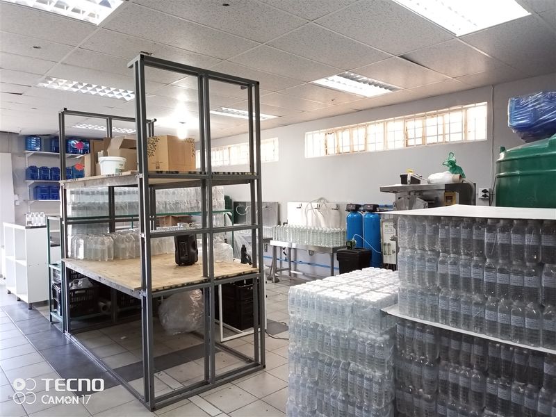 A functional utility and production space featuring industrial shelving, water filtration equipment, stainless steel work surfaces, and tiled flooring.