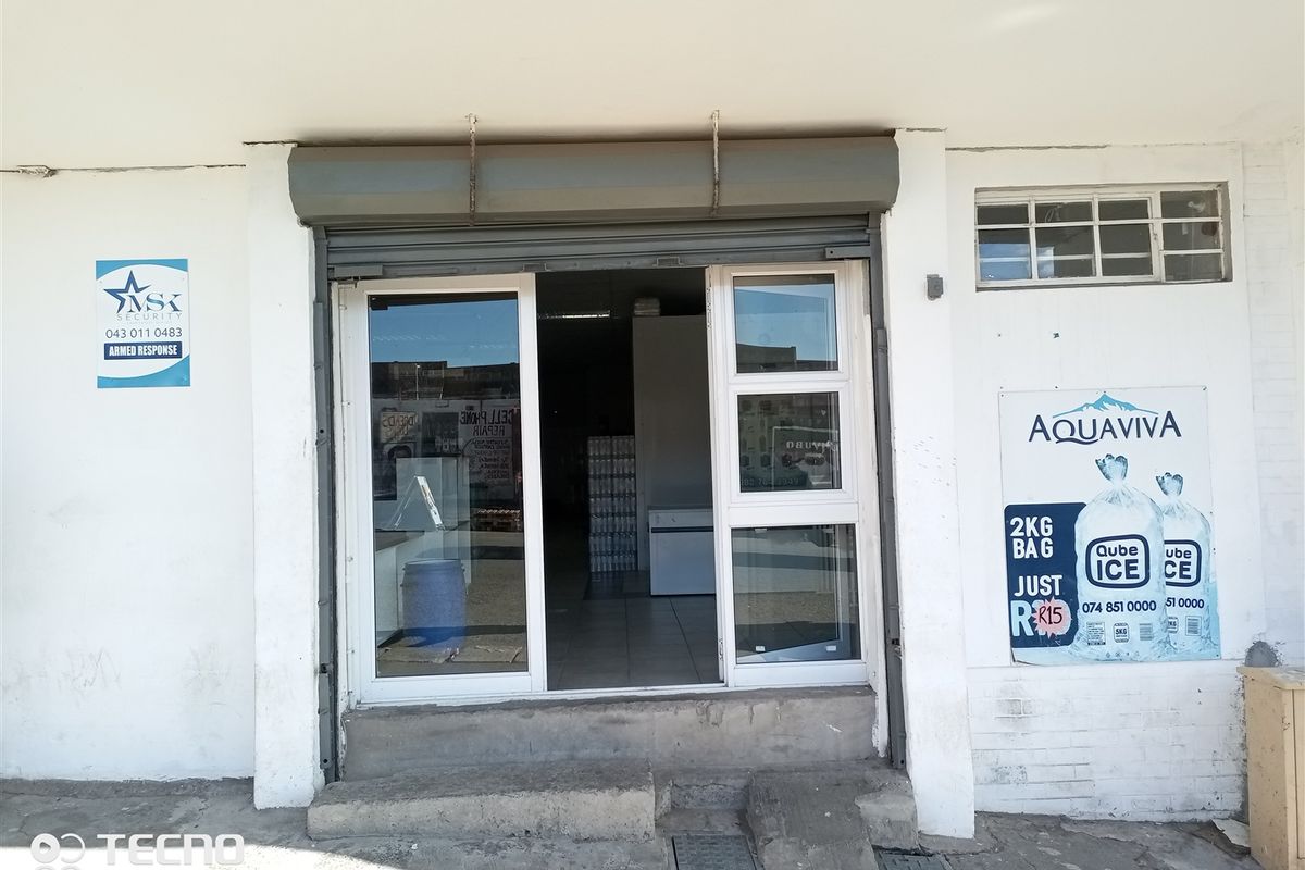 Front entrance of a retail unit featuring a security roller shutter, aluminium glass door, and concrete step access.