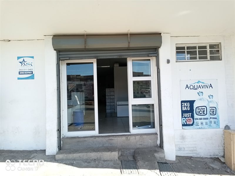 Front entrance of a retail unit featuring a security roller shutter, aluminium glass door, and concrete step access.