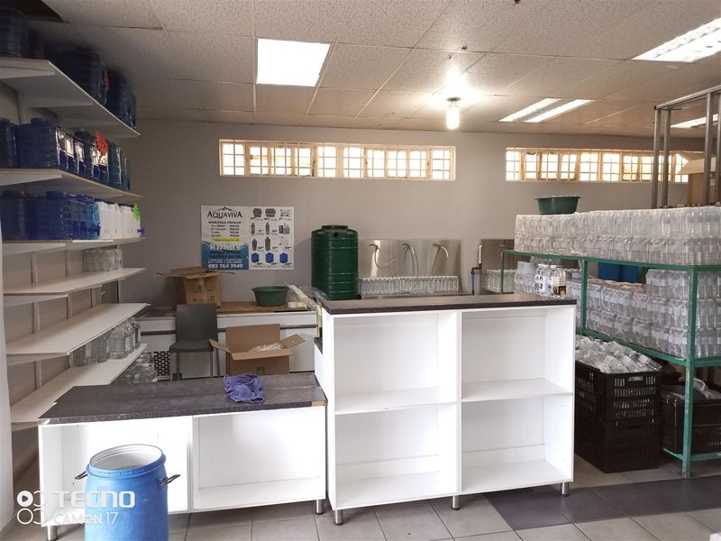 A functional retail utility or processing space featuring tiled floors, suspended ceilings, stainless steel sink, and extensive wall-mounted shelving for storage.