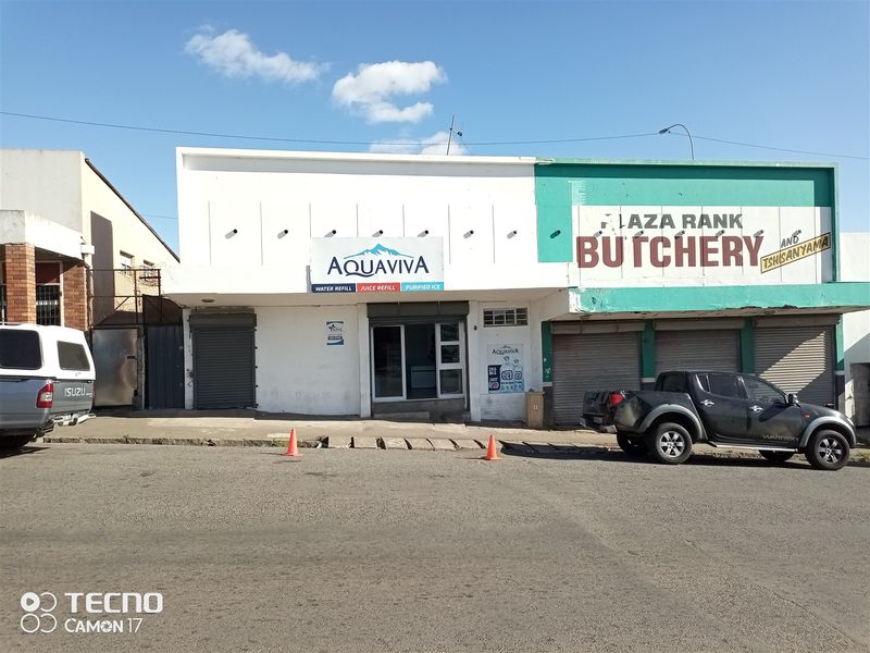 Front facade of a retail property featuring roller shutter doors and a glass entrance, located in a commercial street setting.