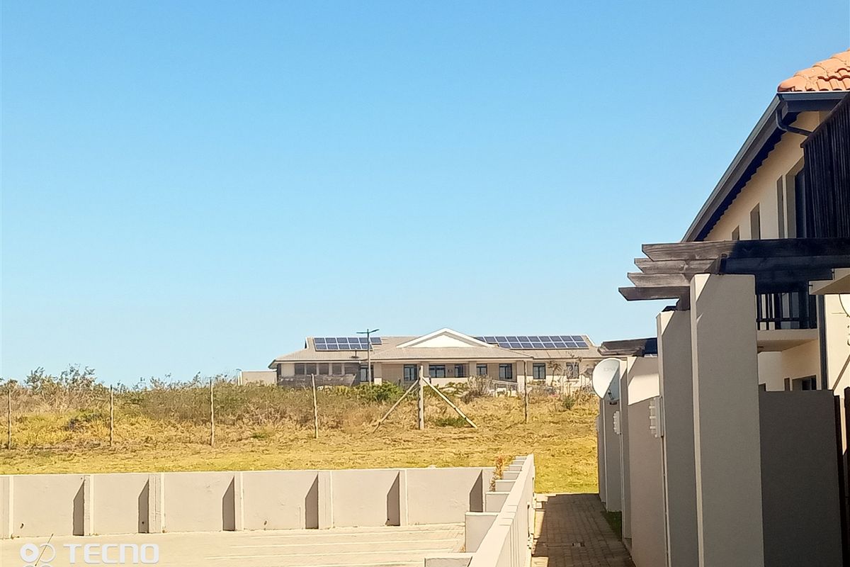 Rear view of the property showing a paved walkway, boundary wall, timber pergola, and solar panels installed on the roof.