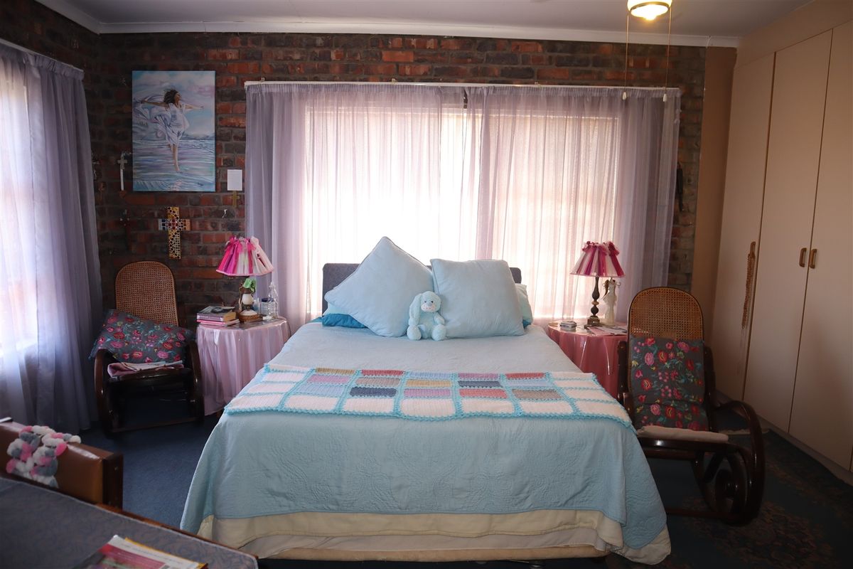 A bedroom featuring an exposed brick feature wall, built-in cupboards, and large windows with sheer curtains.