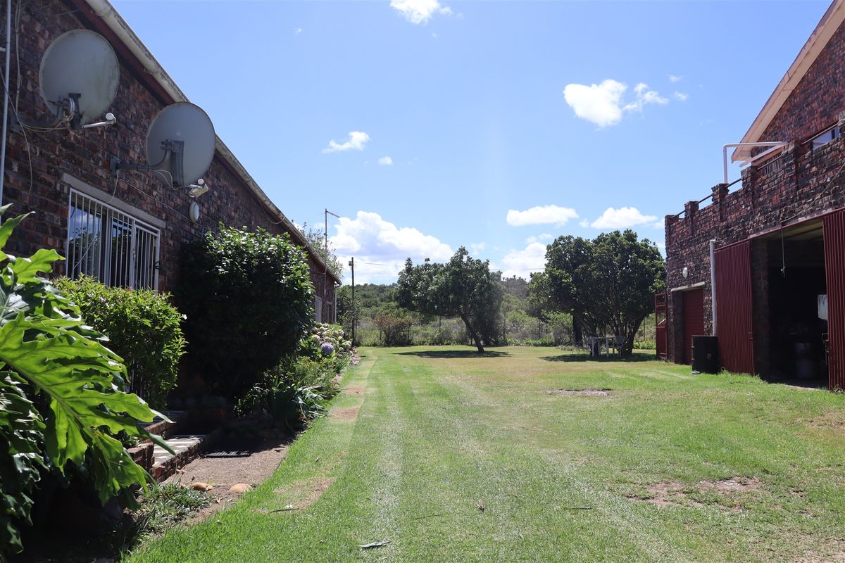 A view of the farm grounds featuring a large lawn area between two brick buildings, including a garage structure and mature trees.