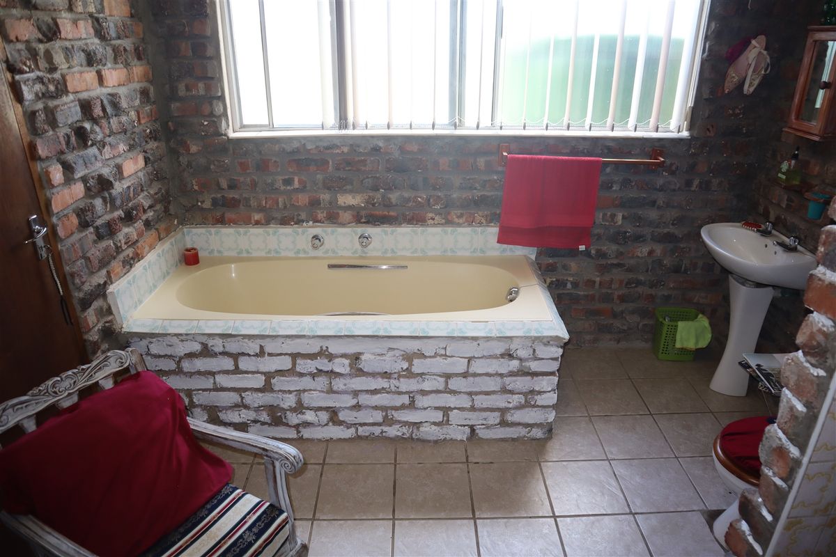 A rustic-style bathroom featuring an exposed brick wall, a built-in bathtub with tiled surround, and a pedestal basin.