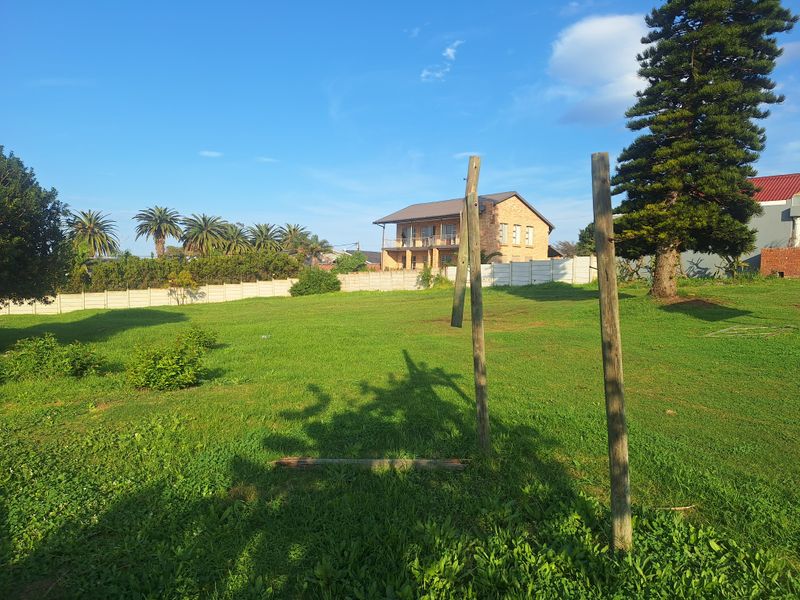 A view of a vacant residential plot featuring a grassy lawn, perimeter precast concrete walling, and mature trees.