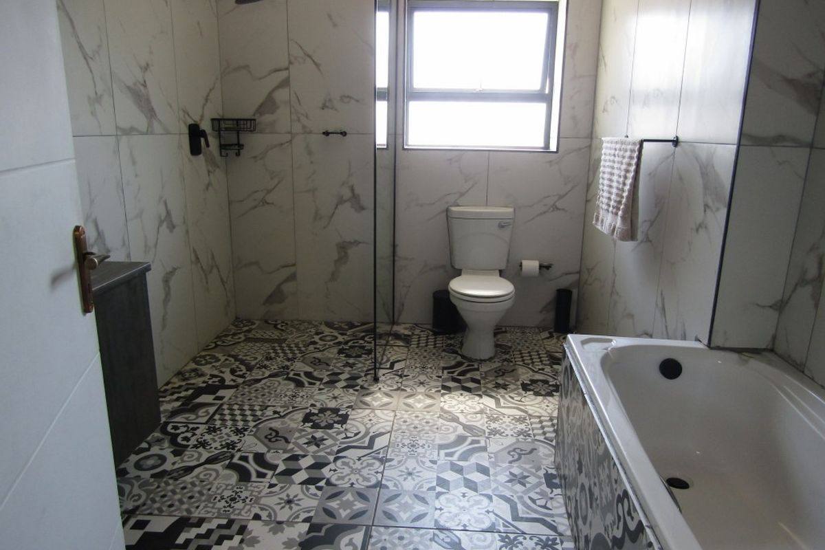 Modern bathroom featuring a walk-in shower with rainfall showerhead, a bathtub, and patterned floor tiles with marble-look wall tiling.