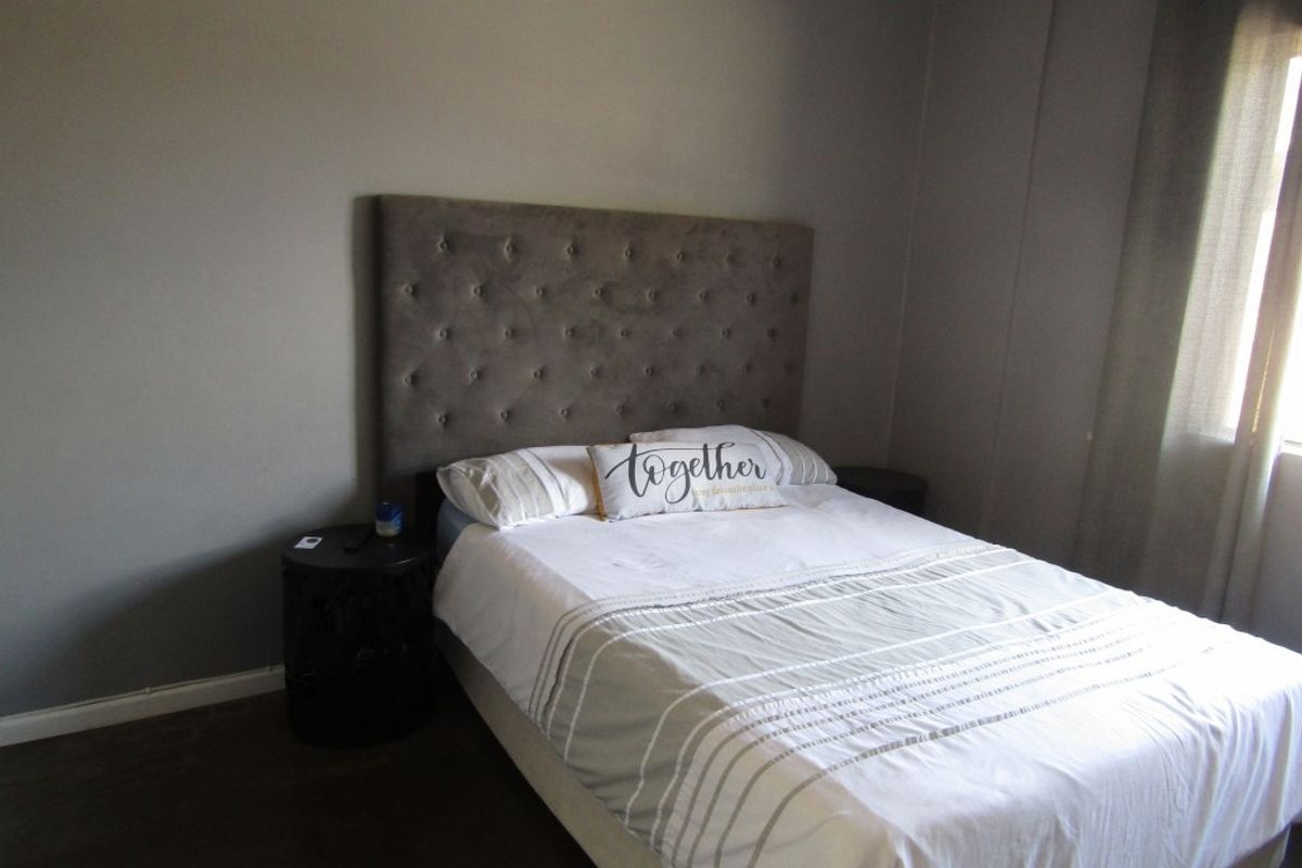 A bedroom featuring neutral grey walls, dark flooring, and a tufted headboard, providing a simple and functional sleeping space.