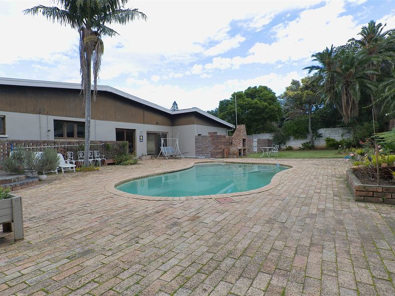 Spacious outdoor entertainment area featuring a swimming pool, brick paved patio, and a built-in brick braai, set within a landscaped garden.